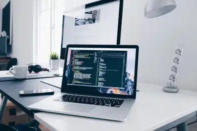 A MacBook with lines of code on its screen on a busy desk